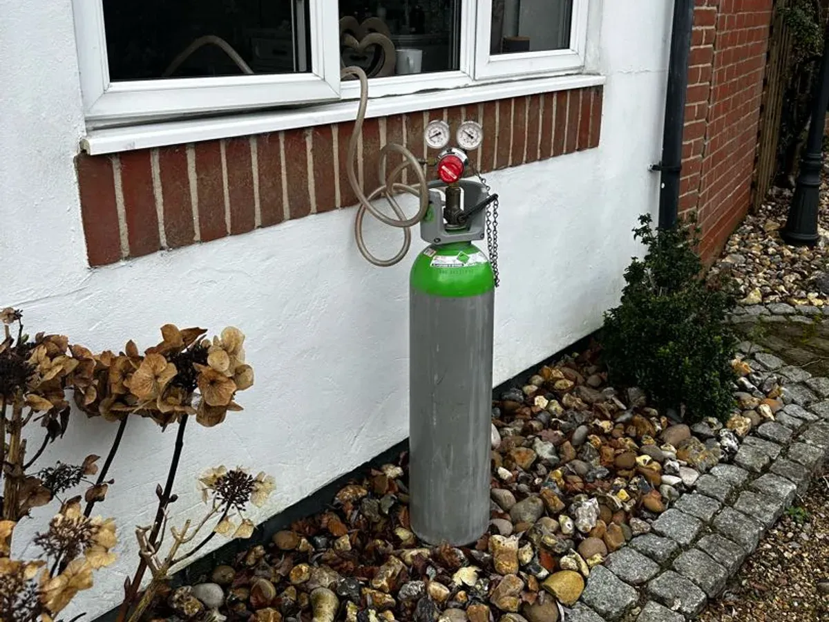 Tracer gas cylinder with its regulator standing against the outside wall of a house during a heating investigation