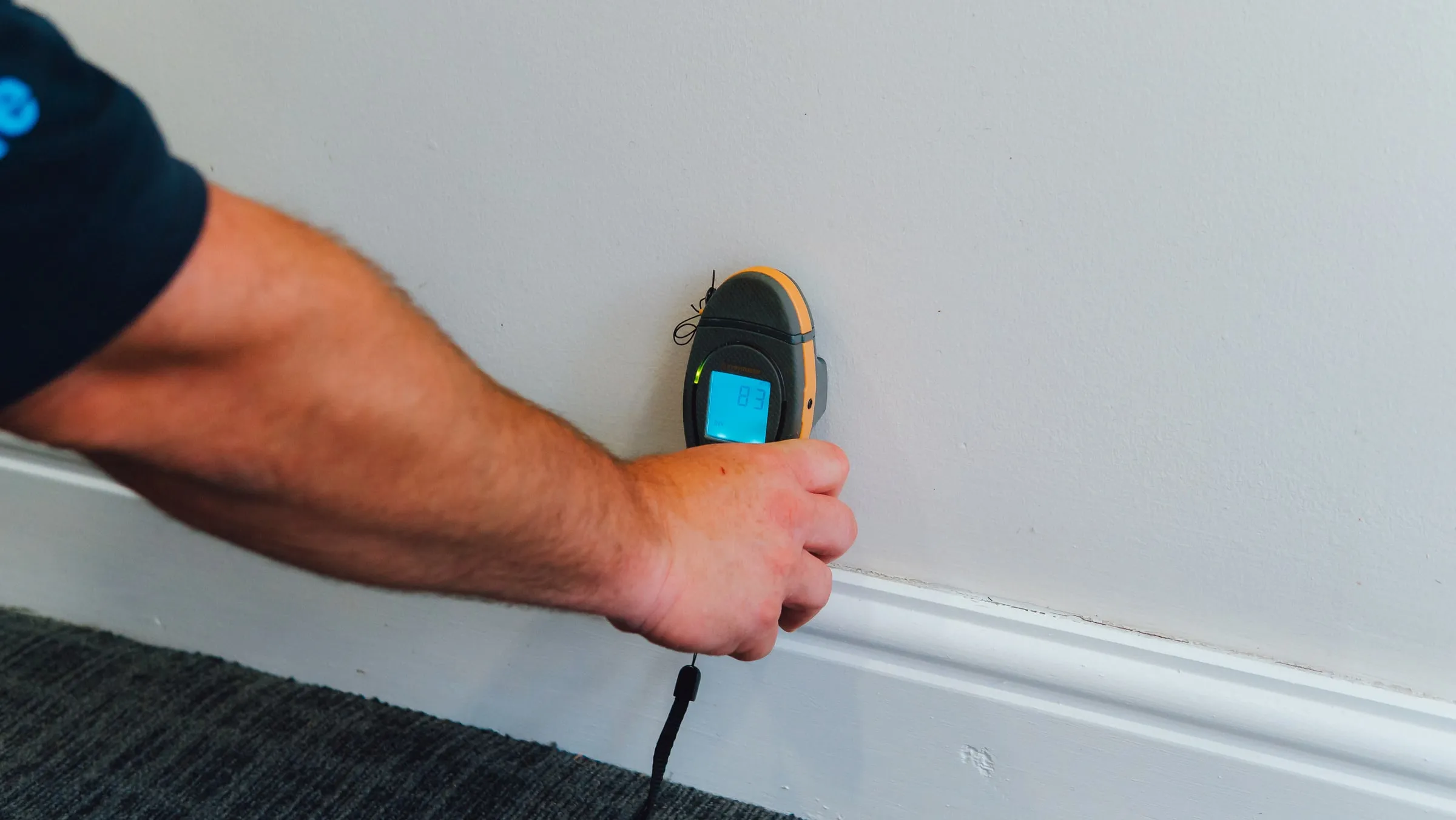 Engineer pressing a moisture meter against a wall just above the skirting board