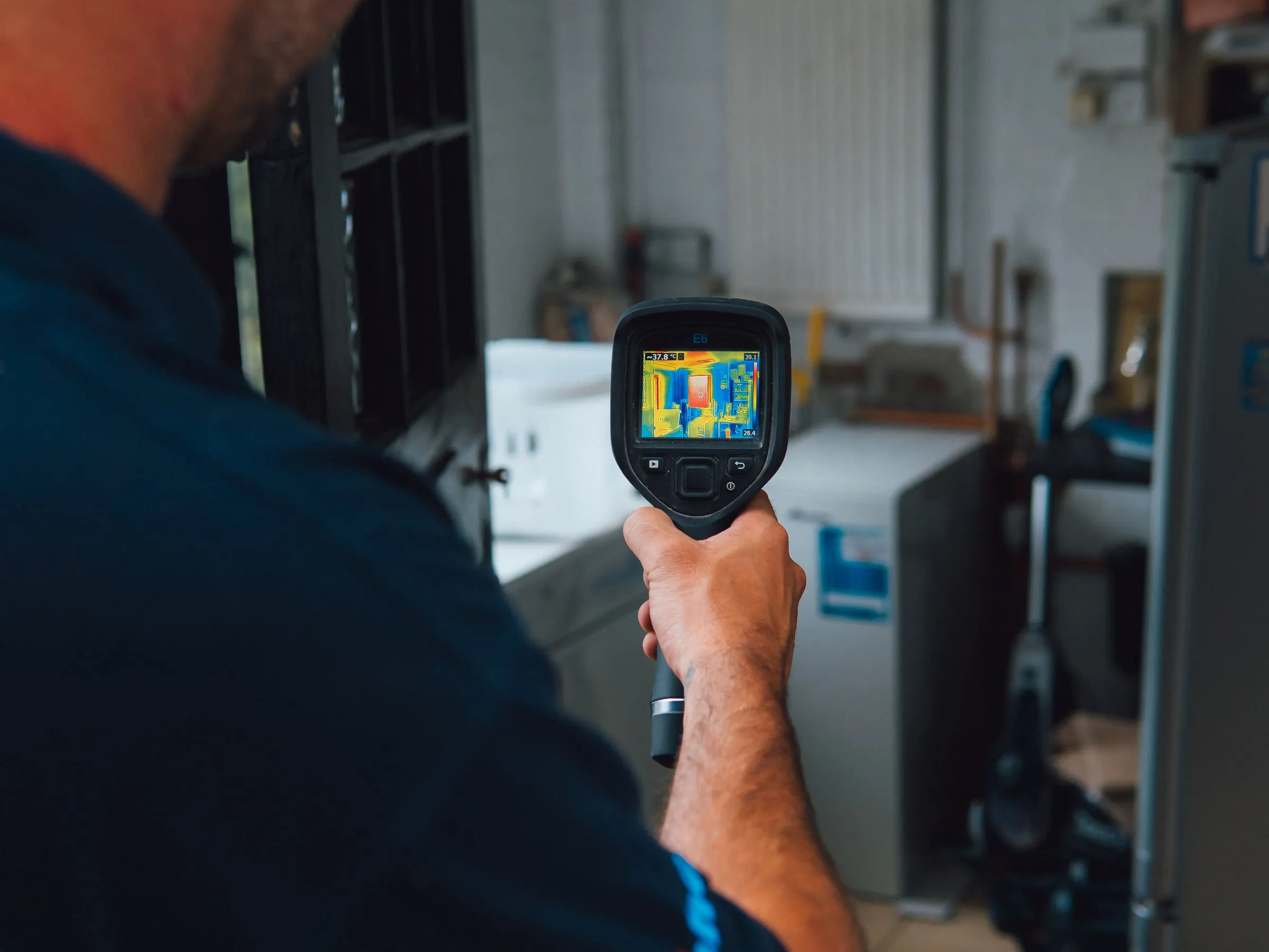 Engineer holding a thermal camera up in a utility room, the screen showing the heat pattern of the pipework
